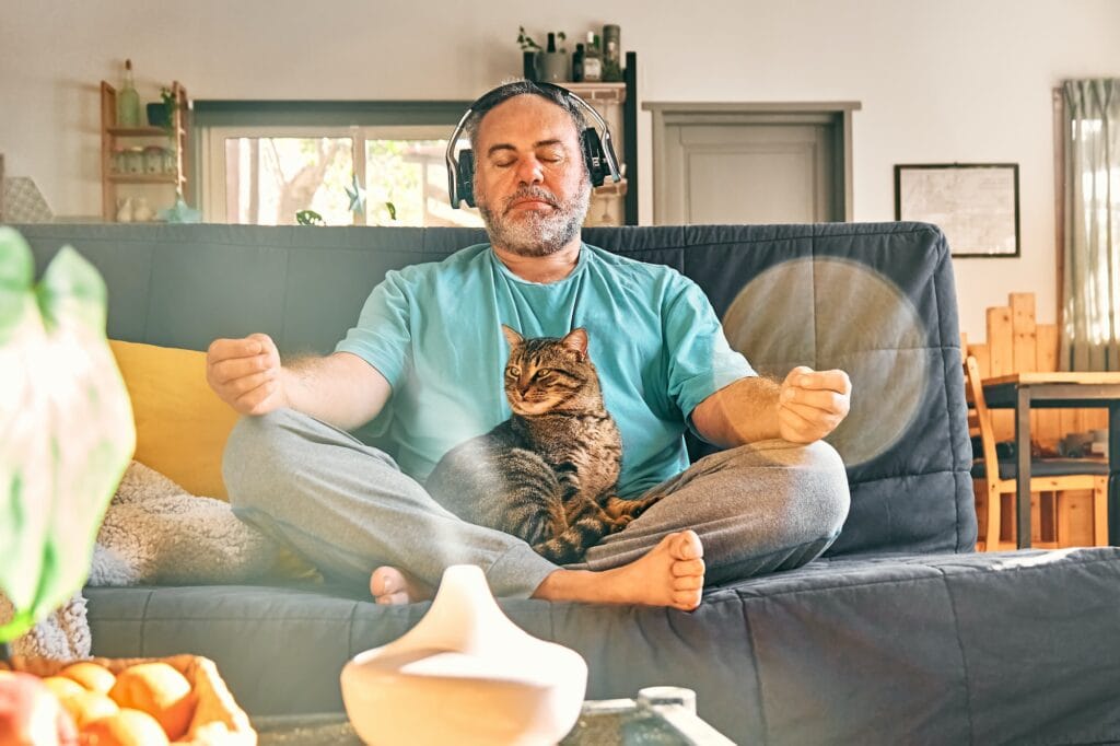 Mature middle-aged overweight man in wireless headphones meditation at home with his cat.