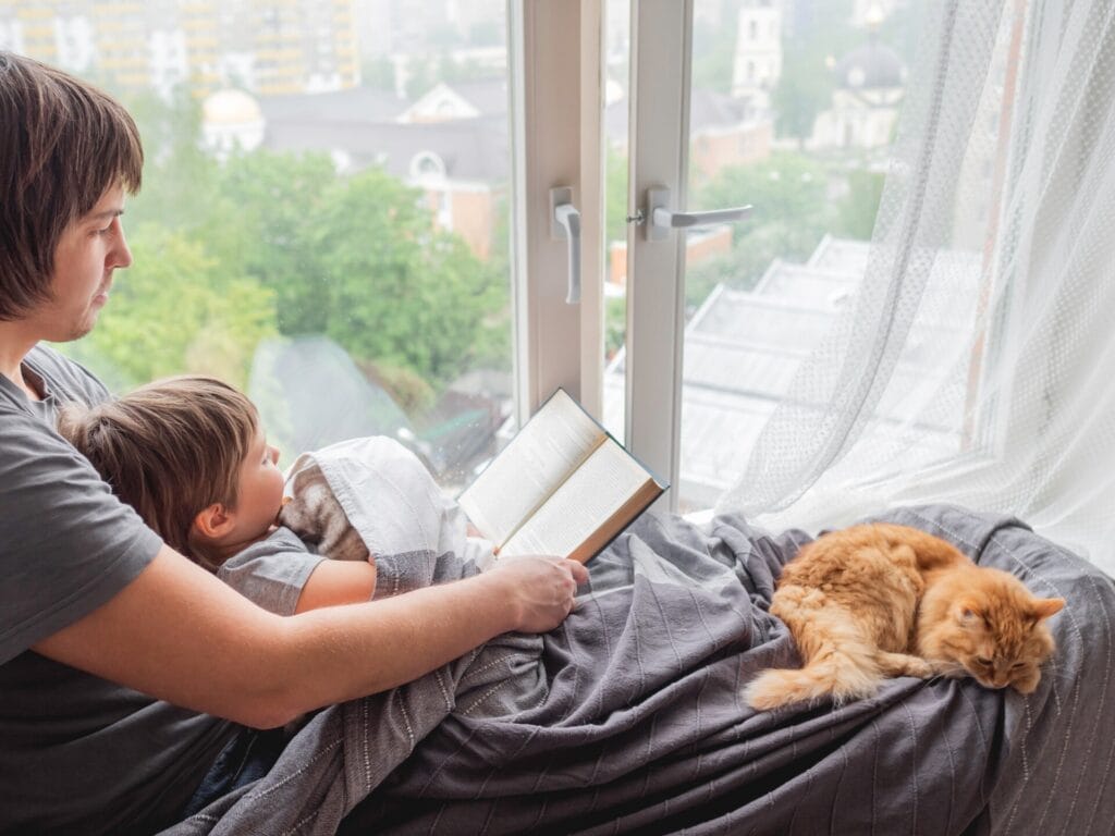 Father reads book to his son and sleepy cat. Family and fluffy pet at home.