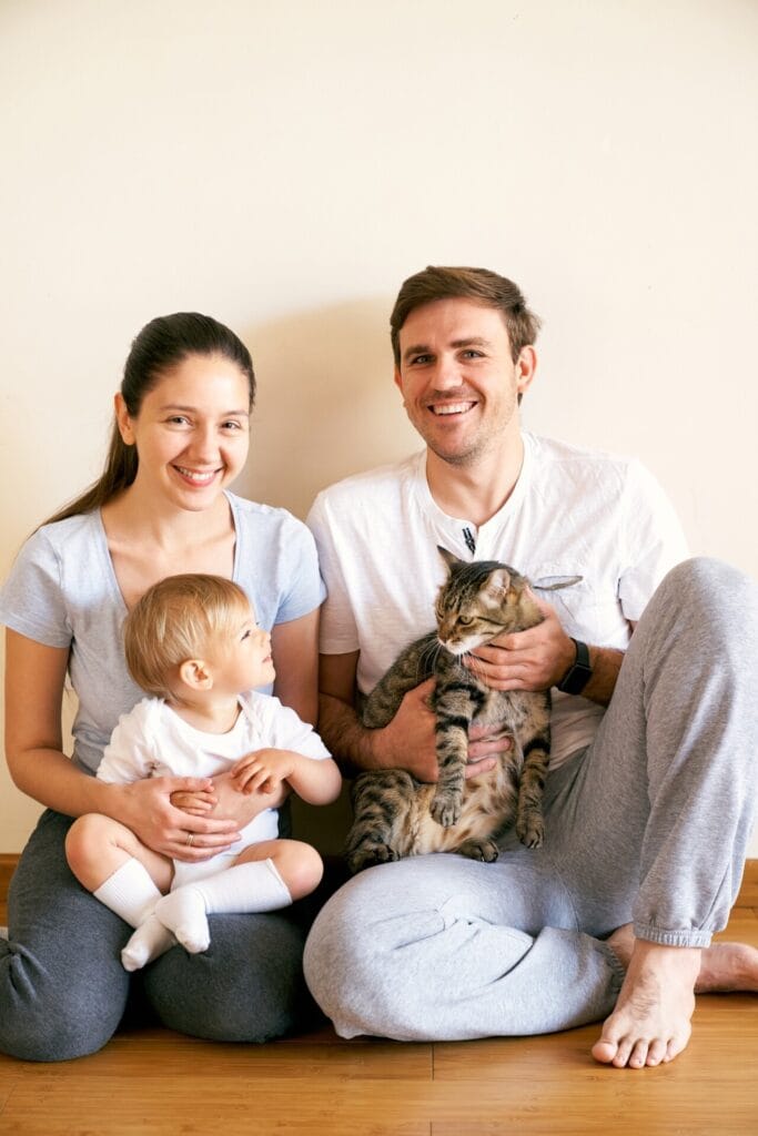 Mom holds a little girl on her lap and dad holds a tabby cat